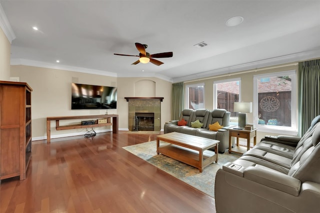 living area with a tiled fireplace, a ceiling fan, crown molding, and wood finished floors