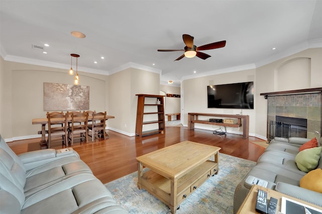 living room with baseboards, a tile fireplace, wood finished floors, and crown molding