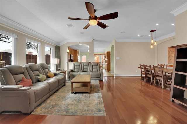 living area with arched walkways, wood finished floors, visible vents, and crown molding