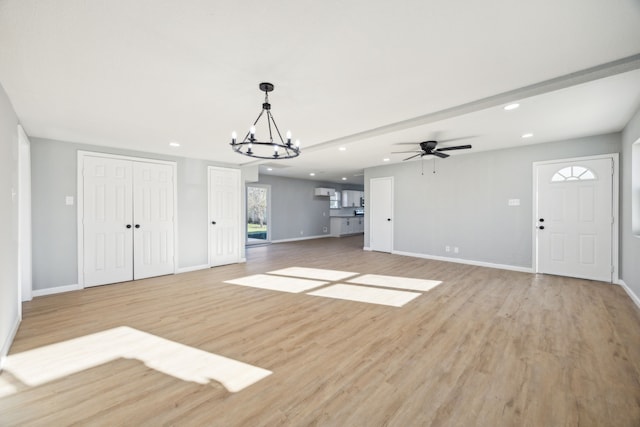 unfurnished living room featuring ceiling fan with notable chandelier, recessed lighting, light wood-type flooring, and baseboards