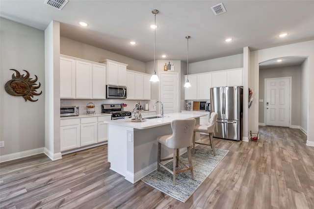 kitchen with arched walkways, stainless steel appliances, a kitchen island with sink, and visible vents