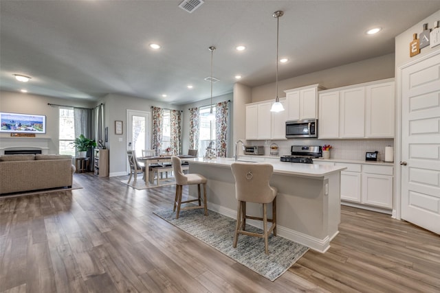 kitchen with stainless steel appliances, tasteful backsplash, visible vents, open floor plan, and wood finished floors