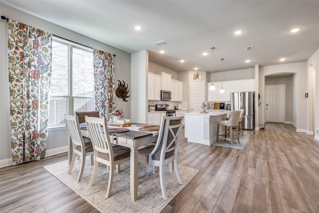 dining room featuring light wood finished floors, visible vents, arched walkways, and recessed lighting