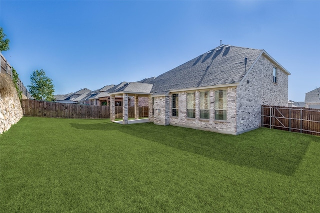 back of property with brick siding, a lawn, a shingled roof, and a fenced backyard