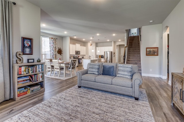 living area featuring arched walkways, dark wood finished floors, baseboards, and stairs