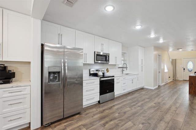 kitchen with wood finished floors, a sink, visible vents, appliances with stainless steel finishes, and backsplash