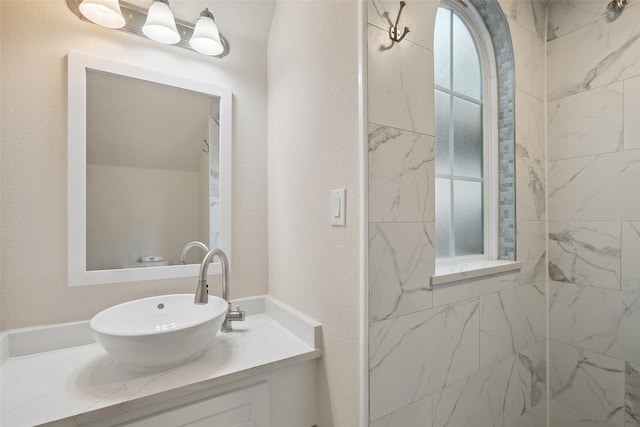 full bathroom featuring a textured wall, a tile shower, and vanity