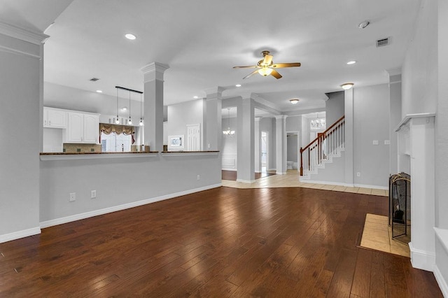 unfurnished living room with ceiling fan with notable chandelier, visible vents, baseboards, wood-type flooring, and decorative columns