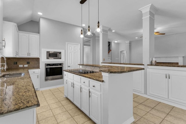 kitchen with decorative columns, dark stone counters, a kitchen island, stainless steel appliances, and a sink