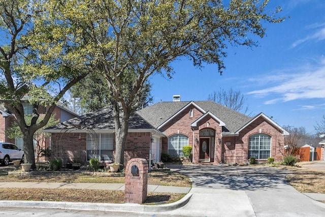 view of front facade with a shingled roof, brick siding, driveway, and an attached garage