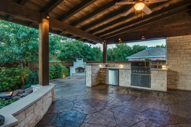 view of patio / terrace featuring an outdoor stone fireplace, grilling area, fence, ceiling fan, and exterior kitchen