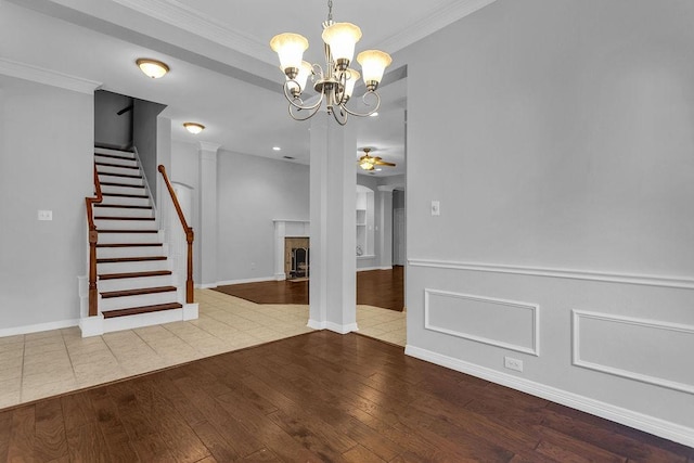 empty room featuring ceiling fan with notable chandelier, a fireplace with flush hearth, stairs, wood-type flooring, and crown molding