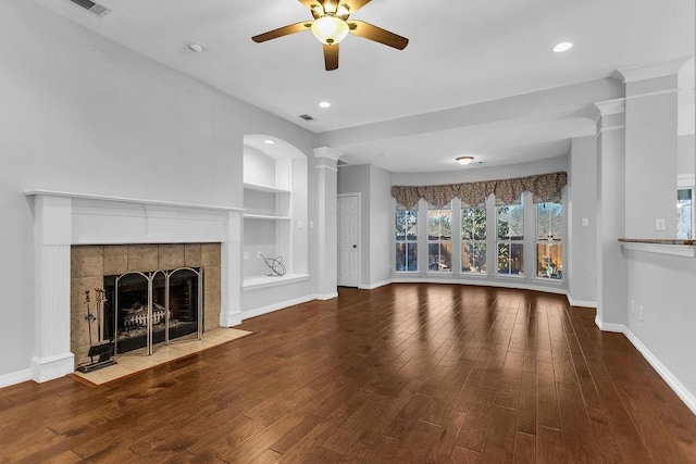 unfurnished living room featuring baseboards, built in features, wood finished floors, ornate columns, and a fireplace