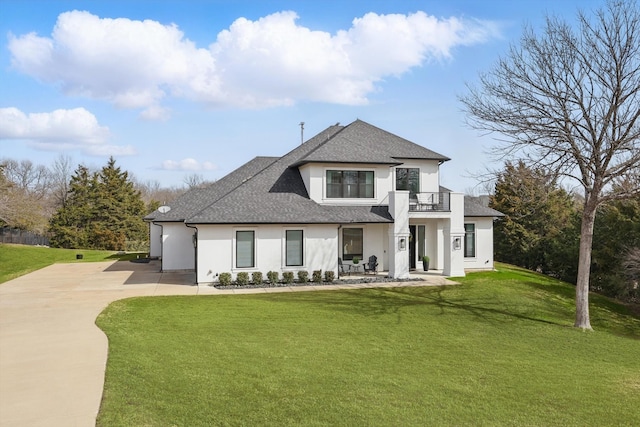 modern inspired farmhouse featuring roof with shingles, stucco siding, a front yard, a balcony, and driveway