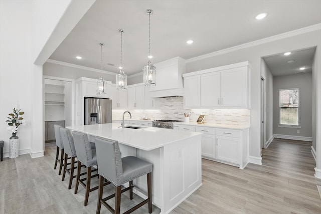 kitchen featuring a breakfast bar area, stainless steel appliances, a sink, white cabinetry, and a center island with sink