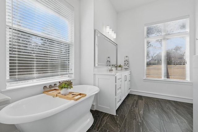 full bathroom with a soaking tub, a healthy amount of sunlight, vanity, and baseboards