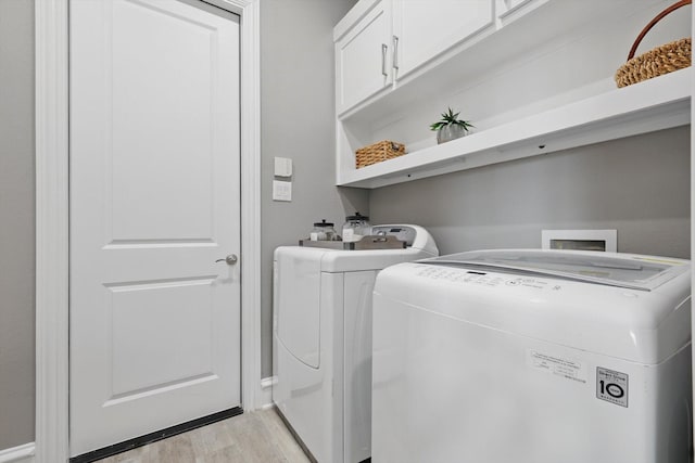 laundry area with cabinet space, light wood-style flooring, and washing machine and clothes dryer