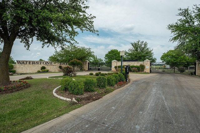 community / neighborhood sign with driveway, a gate, fence, and a yard