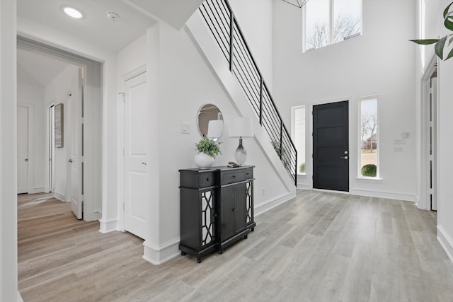 foyer entrance with stairs, a towering ceiling, light wood-style flooring, and baseboards