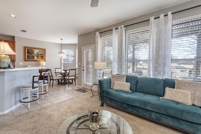 living area featuring light tile patterned floors, visible vents, baseboards, light colored carpet, and ceiling fan