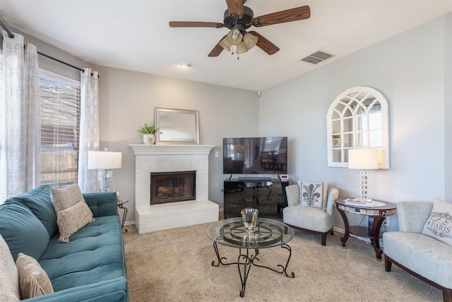 carpeted living area with a brick fireplace, baseboards, visible vents, and a ceiling fan