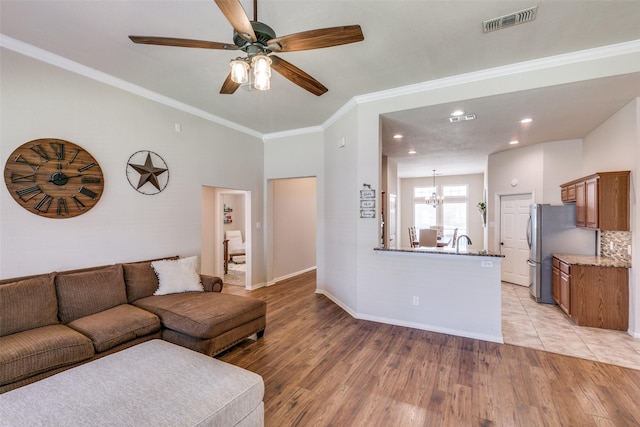 living room with light wood-style flooring, visible vents, baseboards, and ornamental molding