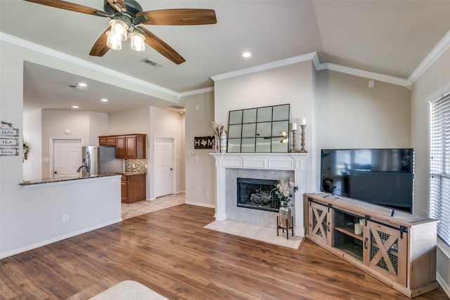 living room with a fireplace, crown molding, visible vents, wood finished floors, and baseboards