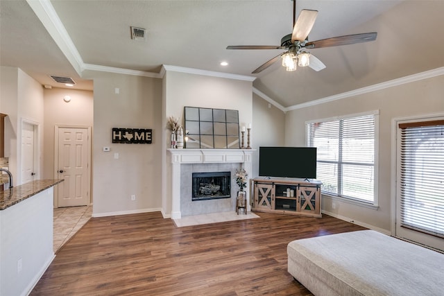 living area with ornamental molding, a tile fireplace, visible vents, and wood finished floors