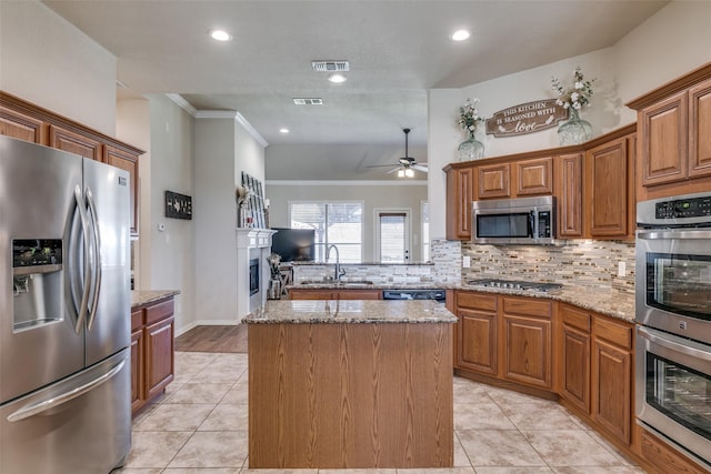 kitchen featuring visible vents, a center island, stainless steel appliances, a fireplace, and a sink