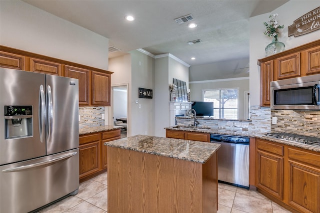 kitchen featuring light stone counters, stainless steel appliances, a sink, visible vents, and a center island