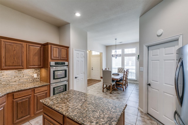 kitchen with brown cabinets, dark stone counters, stainless steel appliances, and decorative backsplash