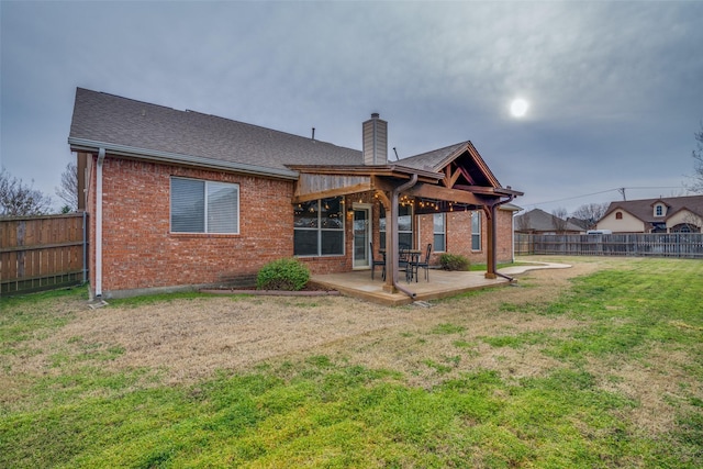 rear view of property with a fenced backyard, a chimney, a yard, a patio area, and brick siding