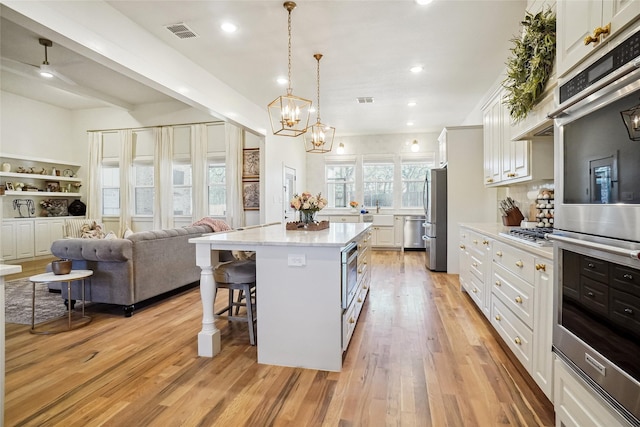 kitchen featuring visible vents, a kitchen island, stainless steel appliances, white cabinets, and a kitchen breakfast bar