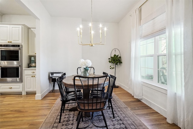 dining space with baseboards, an inviting chandelier, and light wood finished floors