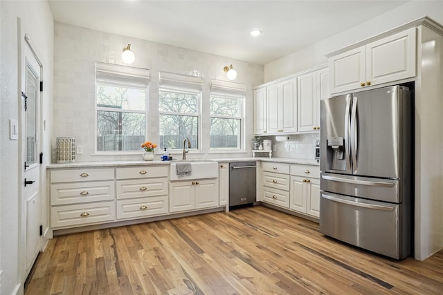 kitchen with appliances with stainless steel finishes, a sink, light countertops, white cabinetry, and light wood-type flooring