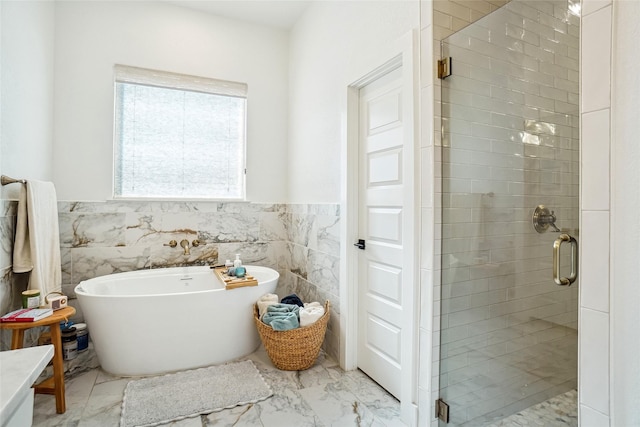 full bathroom featuring tile walls, a stall shower, a wainscoted wall, marble finish floor, and a soaking tub