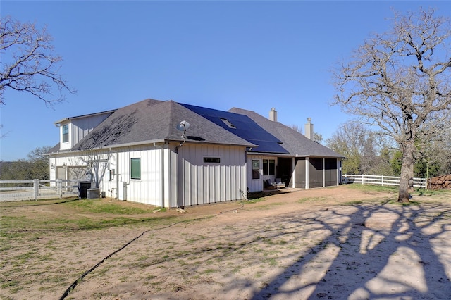 rear view of house featuring board and batten siding, roof with shingles, solar panels, and fence