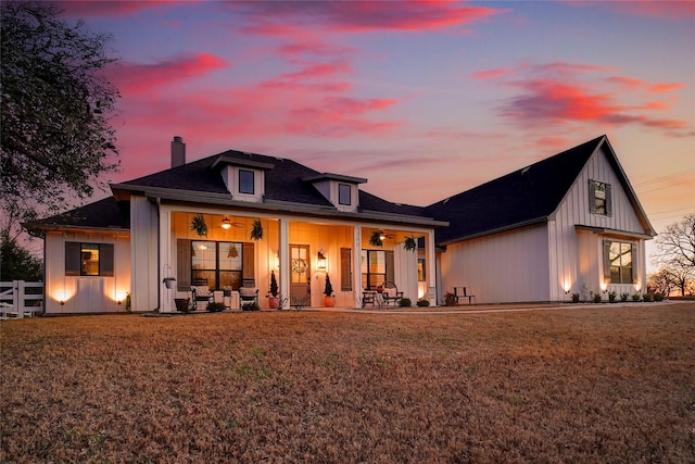 back of property with board and batten siding, a chimney, ceiling fan, and fence