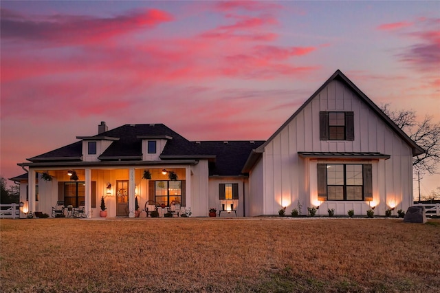 back of house at dusk with board and batten siding, a chimney, a yard, and a shingled roof