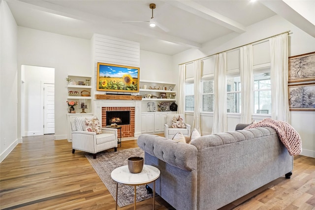 living room with a brick fireplace, beam ceiling, baseboards, ceiling fan, and light wood finished floors