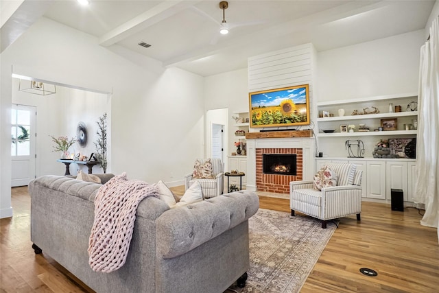 living area featuring visible vents, beam ceiling, built in features, light wood finished floors, and a brick fireplace