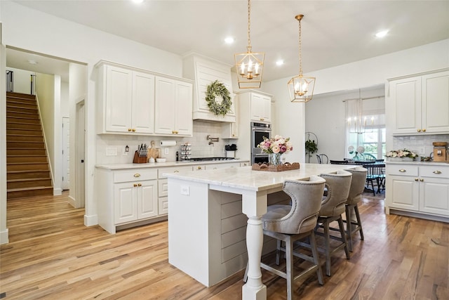 kitchen featuring decorative backsplash, a kitchen island, recessed lighting, light wood finished floors, and a notable chandelier
