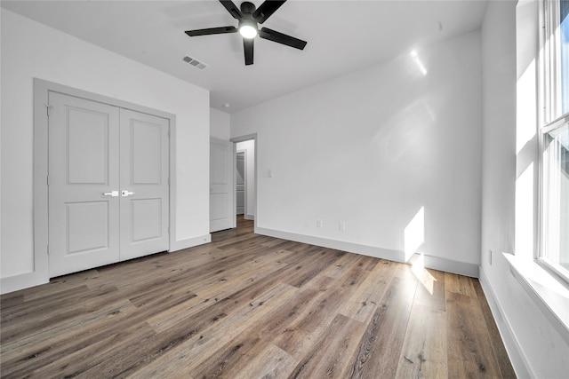 unfurnished bedroom with ceiling fan, visible vents, baseboards, a closet, and hardwood / wood-style floors