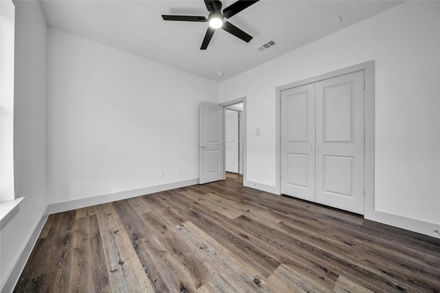 unfurnished bedroom with a closet, wood finished floors, visible vents, and baseboards