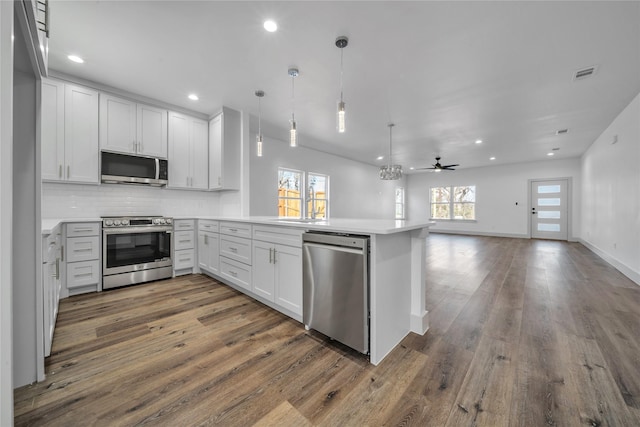 kitchen featuring tasteful backsplash, visible vents, dark wood-style flooring, a peninsula, and stainless steel appliances