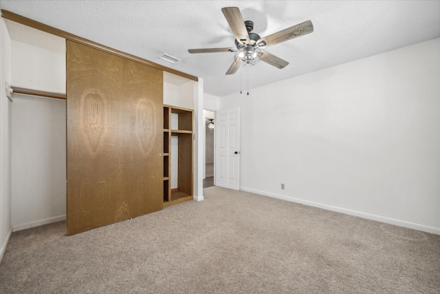 unfurnished bedroom with a textured ceiling, carpet floors, visible vents, baseboards, and a closet