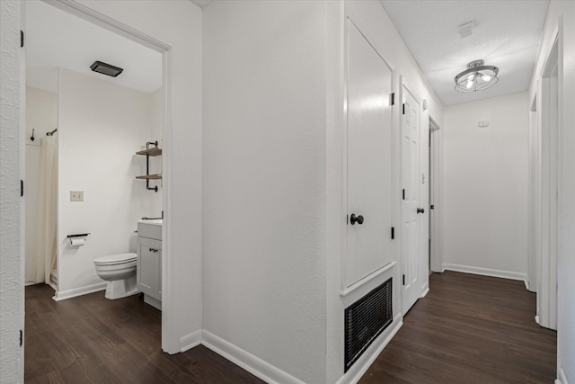 hallway featuring dark wood-style flooring, visible vents, and baseboards