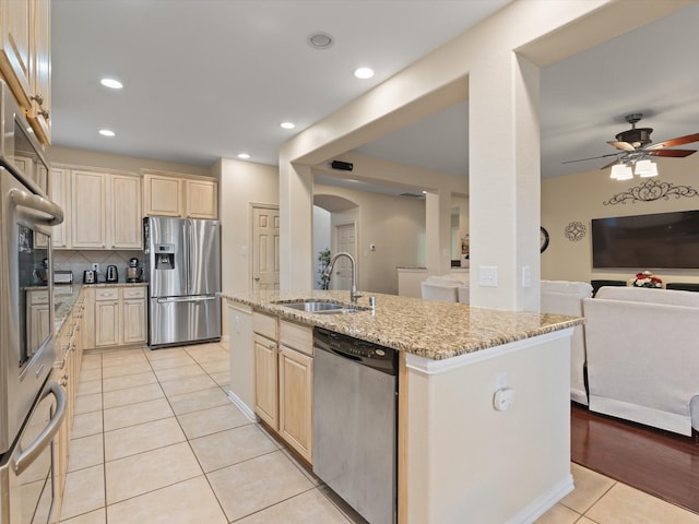 kitchen with light tile patterned floors, stainless steel appliances, open floor plan, a sink, and light stone countertops