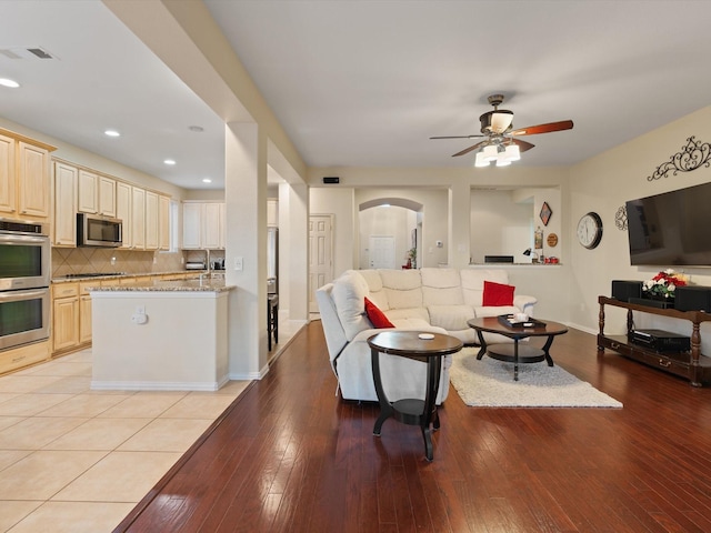 living area featuring light wood-type flooring, visible vents, arched walkways, and a ceiling fan