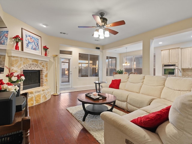 living room featuring visible vents, dark wood-type flooring, a healthy amount of sunlight, a fireplace, and ceiling fan with notable chandelier